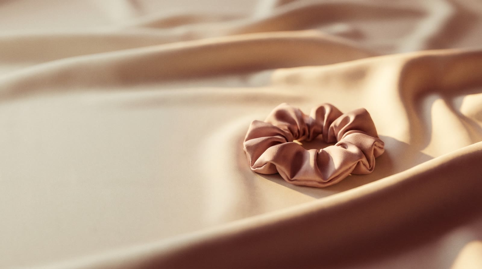 Blush silk scrunchie resting on flowing cream silk — hero preview still